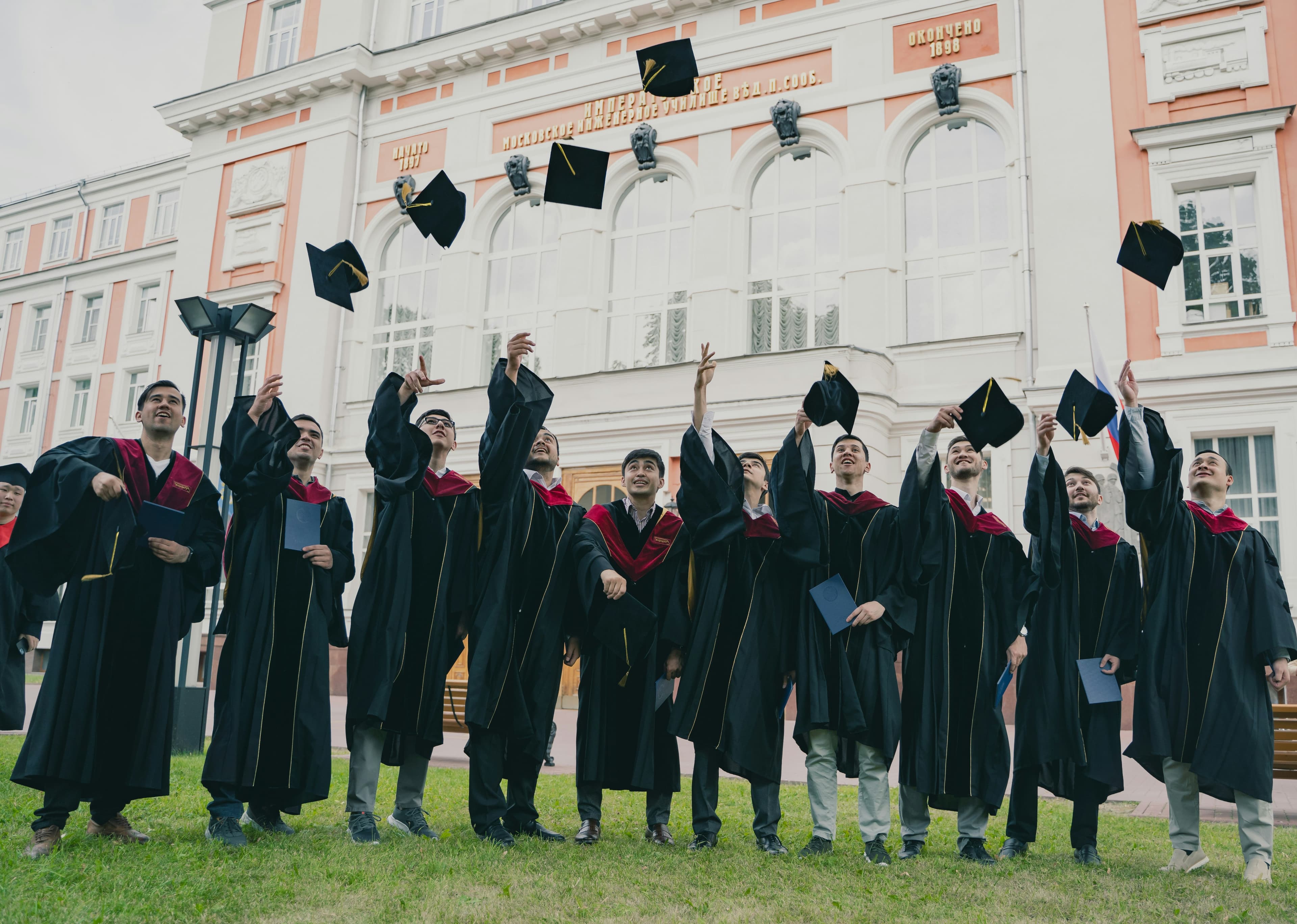 University graduates throwing their caps into the air outside a campus building.